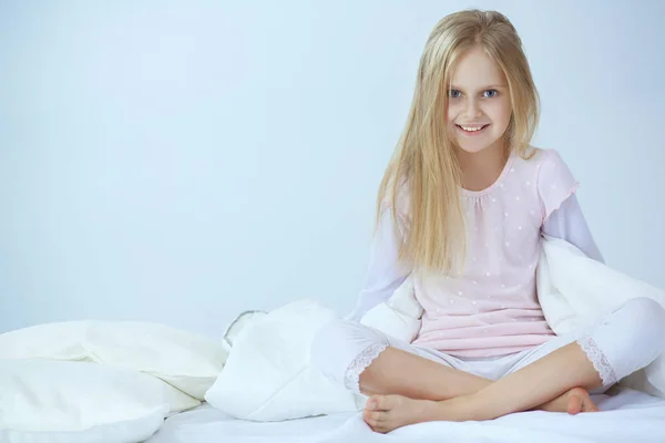 Das kleine Mädchen im Schlafzimmer sitzt auf dem Bett. kleines Mädchen trägt Schlafanzug und sitzt im Bett — Stockfoto