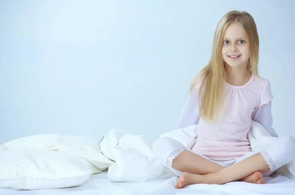 Das kleine Mädchen im Schlafzimmer sitzt auf dem Bett. kleines Mädchen trägt Schlafanzug und sitzt im Bett — Stockfoto