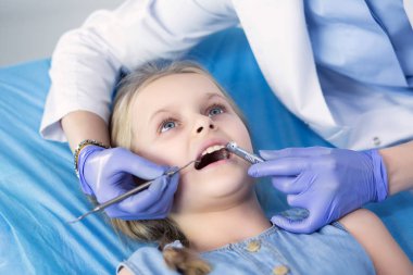 Küçük kız dişçi ofisinde oturuyor.