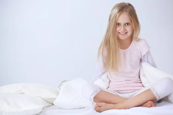 Das kleine Mädchen im Schlafzimmer sitzt auf dem Bett. kleines Mädchen trägt Schlafanzug und sitzt im Bett — Stockfoto