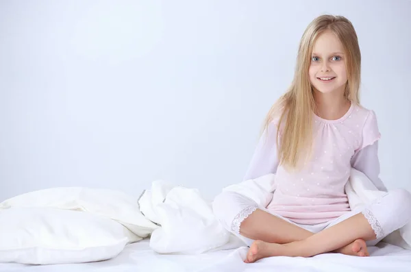 Liten flicka i sovrummet sitter på sängen. Lilla flickan bär en pyjamas och sitter i sängen — Stockfoto