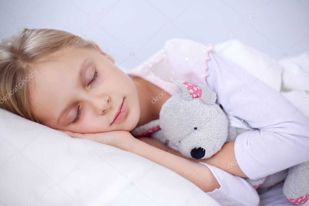 Child little girl sleeps in the bed with a toy teddy bear