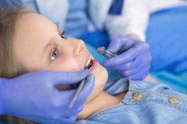 Küçük kız dişçi ofisinde oturuyor.