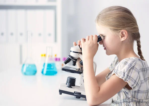 Школярка дивиться через мікроскоп на уроці науки — стокове фото