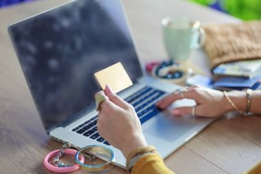 Kredi kartı tutan ve dizüstü bilgisayar kullanan genç bir kadın. Çevrimiçi alışveriş kavramı