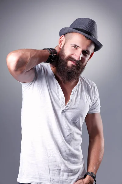 Retrato de homem barbudo bonito de chapéu em pé, isolado sobre fundo cinza — Fotografia de Stock