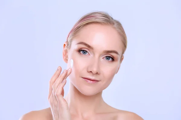 Portret van een vrolijke glimlachende mooie jonge vrouw die de huid aanraakt of crème aanbrengt, geïsoleerd over een witte achtergrond — Stockfoto