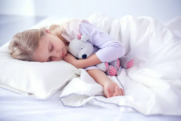 Criança menina dorme na cama com um brinquedo ursinho de pelúcia — Fotografia de Stock