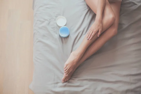 Bella donna seduta sul letto e applicare la crema sulle gambe — Foto Stock