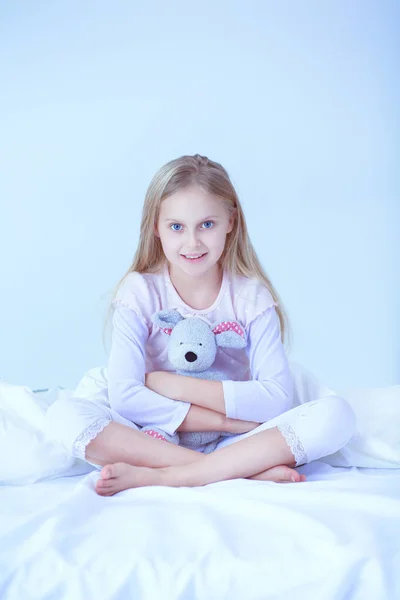 La niña en el dormitorio está sentada en la cama. La niña está usando un pijama y sentada en la cama —  Fotos de Stock