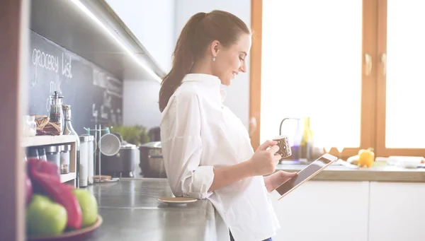 Mujer joven usando la tableta en la cocina en casa y beber café — Foto de Stock