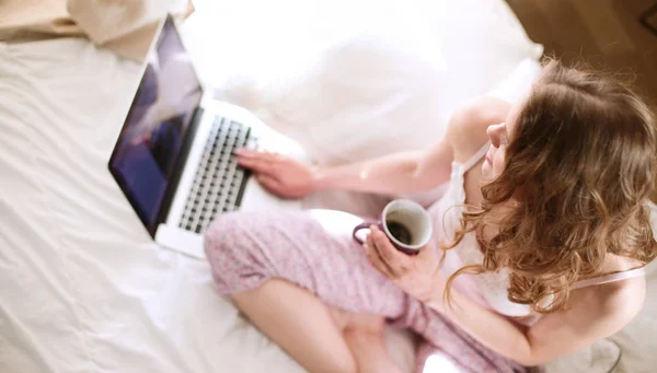 Jeune belle femme assise dans le lit avec ordinateur portable — Photo