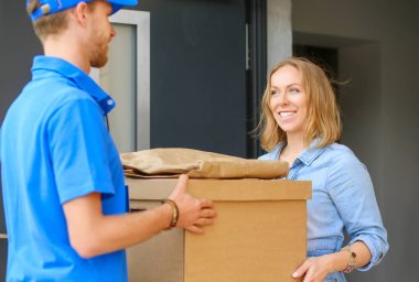 Mavi üniformalı gülümseyen kurye servis konseptine paket kutusu teslim eden teslimatçı. Mavi üniformalı gülümseyen teslimatçı.