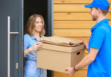 Mavi üniformalı gülümseyen kurye servis konseptine paket kutusu teslim eden teslimatçı. Mavi üniformalı gülümseyen teslimatçı.