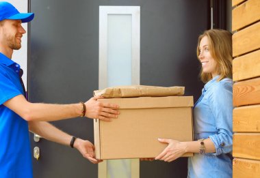 Mavi üniformalı gülümseyen kurye servis konseptine paket kutusu teslim eden teslimatçı. Mavi üniformalı gülümseyen teslimatçı.