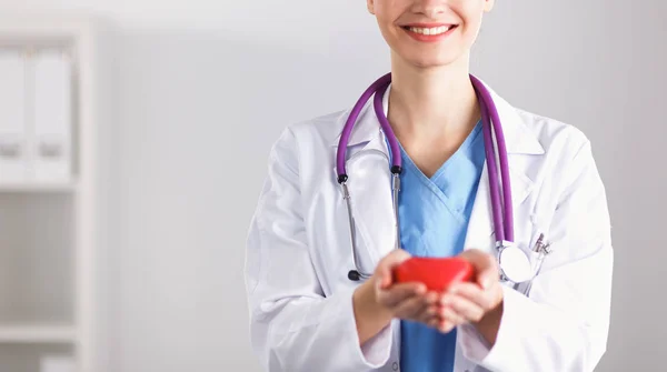 Mujer joven doctora sosteniendo un corazón rojo, parada en el hospital — Foto de Stock