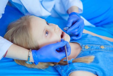 Küçük kız dişçi ofisinde oturuyor.