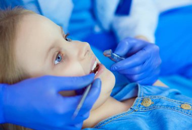 Küçük kız dişçi ofisinde oturuyor.