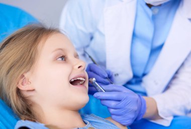 Küçük kız dişçi ofisinde oturuyor.