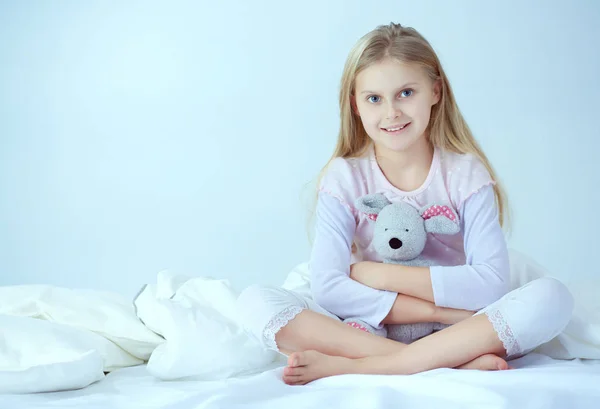 La niña en el dormitorio está sentada en la cama. La niña está usando un pijama y sentada en la cama —  Fotos de Stock