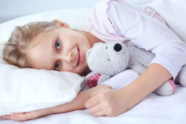 Barn lilla flicka sover i sängen med en leksak nallebjörn — Stockfoto