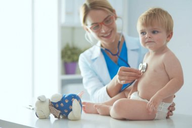 Kadın doktor, klinikte steteskoplu bir çocuğu dinliyor.