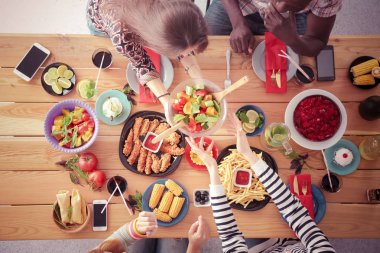 Ahşap masada otururken birlikte yemek yiyen bir grup insanın üst düzey görüntüsü. Masada yemek var. İnsanlar fast food yiyor..