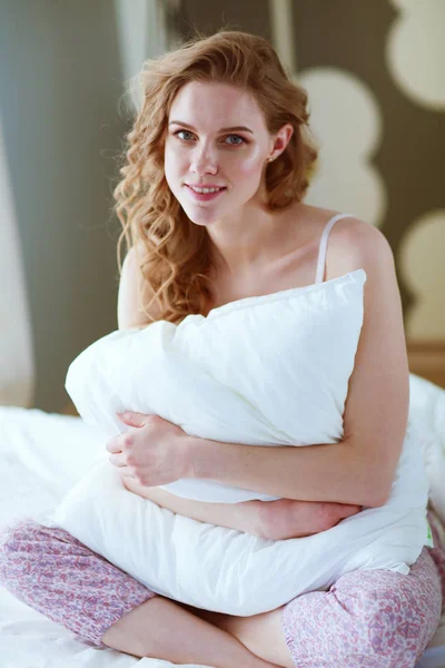 Young woman holding a pillow while sitting on her bed. — Stock Photo, Image