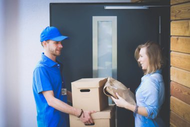 Mavi üniformalı gülümseyen kurye servis konseptine paket kutusu teslim eden teslimatçı.