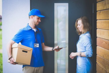 Mavi üniformalı gülümseyen kurye servis konseptine paket kutusu teslim eden teslimatçı.