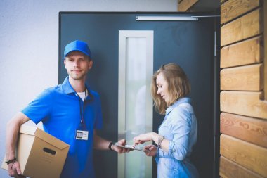 Mavi üniformalı gülümseyen kurye servis konseptine paket kutusu teslim eden teslimatçı.