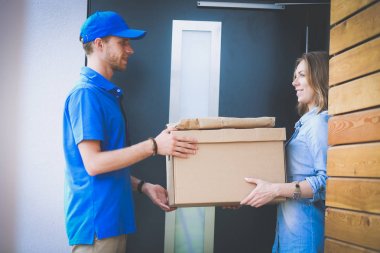 Mavi üniformalı gülümseyen kurye servis konseptine paket kutusu teslim eden teslimatçı.