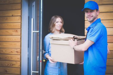 Mavi üniformalı gülümseyen kurye servis konseptine paket kutusu teslim eden teslimatçı.
