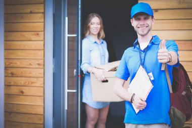 Mavi üniformalı gülümseyen kurye servis konseptine paket kutusu teslim eden teslimatçı.