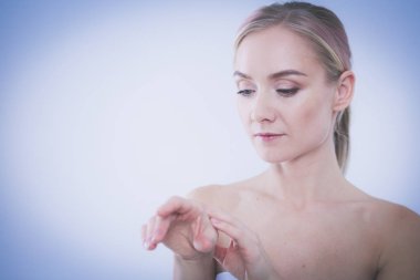 Mutlu gülümseyen genç bir kadının portresi tenine dokunuyor ya da krem sürüyor, beyaz arka planda izole edilmiş.