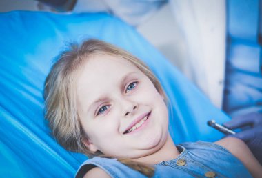 Küçük kız dişçi ofisinde oturuyor.