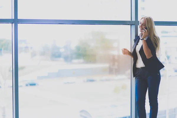 Mujer de negocios de pie contra la ventana de la oficina hablando por teléfono móvil —  Fotos de Stock