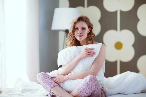 Junge Frau hält ein Kissen während sie auf ihrem Bett sitzt — Stockfoto