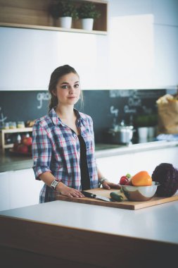Masanın yanındaki mutfakta sebze doğrayan genç bir kadın.