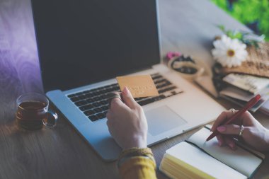 Kredi kartı tutan ve dizüstü bilgisayar kullanan genç bir kadın. Çevrimiçi alışveriş kavramı