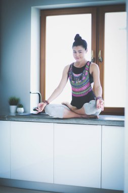 Lotus pozisyonunda mutfak masasında oturan genç güzel kadın