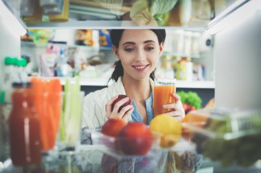 Sağlıklı yiyecek, sebze ve meyvelerle dolu açık buzdolabının yanında duran kadın portresi.