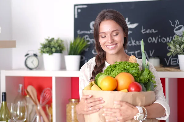 Jovem mulher segurando supermercado saco de compras com legumes .Standing na cozinha — Fotografia de Stock