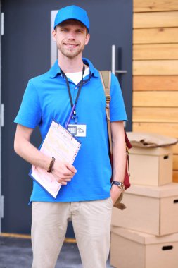 Mavi üniformalı gülümseyen kurye servis konseptine paket kutusu teslim eden teslimatçı.