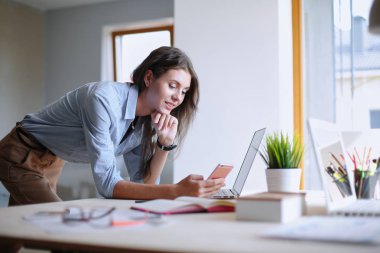 Dizüstü bilgisayar ekranına bakarak office tablosunda oturan genç kadın