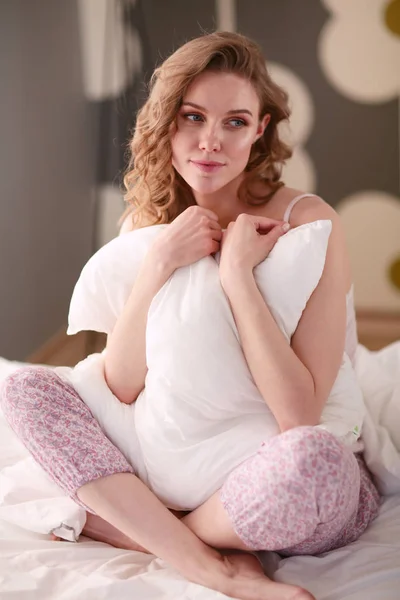 Νέα γυναίκα που κρατά ένα μαξιλάρι, ενώ κάθεται στο κρεβάτι της — Φωτογραφία Αρχείου