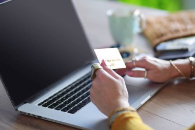 Kredi kartı tutan ve dizüstü bilgisayar kullanan genç bir kadın. Çevrimiçi alışveriş kavramı