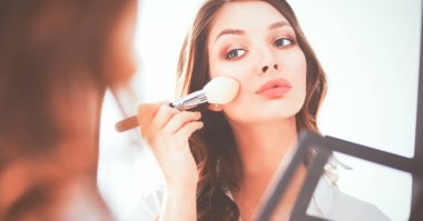 Genç ve güzel bir kadın aynanın yanında makyaj yapıyor.