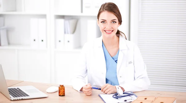 Красивая молодая улыбающаяся женщина-врач сидит за столом и пишет:. — стоковое фото