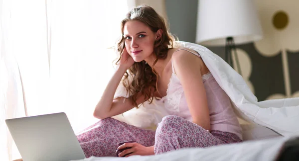 Young beautiful woman sitting in bed with laptop — Stock Photo, Image